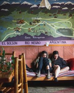 dos personas sentadas en una cama bajo un mapa en Ankatu Hostel en El Bolsón