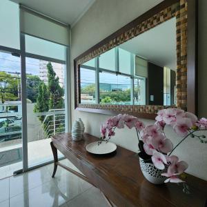 a vase of flowers on a table in a room with a mirror at Atlantis Residence in Vitória