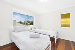 two beds in a white room with a window at Ultimate Burleigh Beach House Family Retreat! - 5 BEDROOMS in Gold Coast