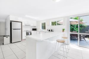 a white kitchen with a large white counter and stools at Ultimate Burleigh Beach House Family Retreat! - 5 BEDROOMS in Gold Coast
