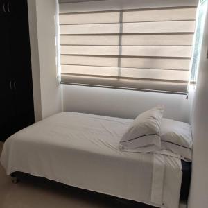 1 cama con sábanas y almohadas blancas frente a una ventana en lujoso apartamento, en Ricaurte