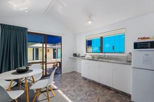 a kitchen with white cabinets and a table and chairs at Kaiteriteri Reserve Cabins in Kaiteriteri