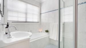 a white bathroom with a sink and a bath tub at Palm Breeze in Kiama