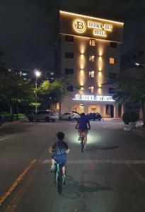 two people riding bikes down a street in front of a hotel at Browndot Hotel Mokpo Gotbawi in Mokpo