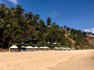 einen Strand mit Sonnenschirmen, Stühlen und Palmen in der Unterkunft Casa Pirambu in Pipa