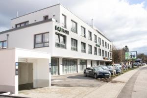 een wit gebouw met auto's geparkeerd op een parkeerplaats bij ING Hotel by WMM Hotels in Ingolstadt