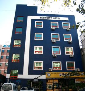 Ekonomy Hotel في موكبو: مبنى ازرق وابيض فيه سيارات تقف امامه