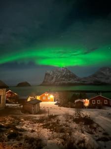 an aurora shines in the sky over a house at Haukland beach panorama in Offersøya