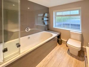 a bathroom with a tub and a toilet and a window at BLUNSDON LODGE - Spacious Bungalow, High Speed Wi-Fi, Free Private Parking, Garden in Swindon