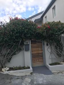 a white house with a wooden door and red flowers at Seaforth Suite in Simonʼs Town
