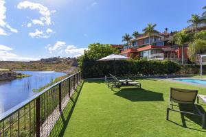 einen Balkon mit Stühlen und einem Regenschirm neben einem Fluss in der Unterkunft Los Dragos 13 Salobre by VillaGranCanaria in Maspalomas