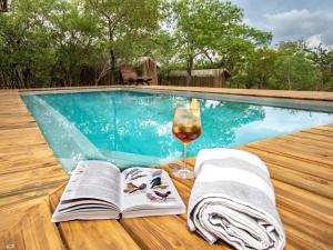 a book and a glass of wine next to a swimming pool at Langa Langa Tented Safari Camp in Huntingdon