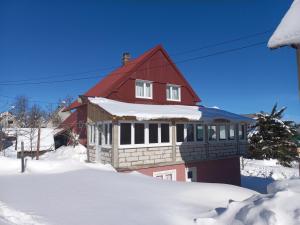 una casa con un tetto rosso nella neve di Apartmani Sobe Sljivancanin a Žabljak