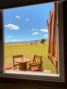 una ventana con una mesa y sillas con vistas a un campo en Cabañas La Esperanza en Tornquist
