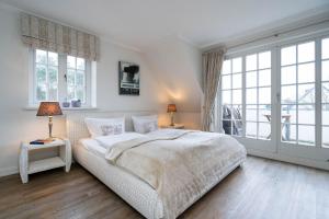 a white bedroom with a large bed and windows at Hermes Hü in Wenningstedt