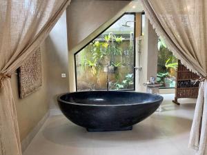 a large black bath tub in a bathroom with a window at Chakra Living Ubud in Ubud
