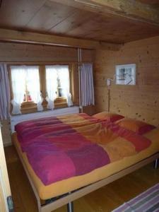 a large bed in a wooden room with windows at Chalet Flädermuus in Frutigen