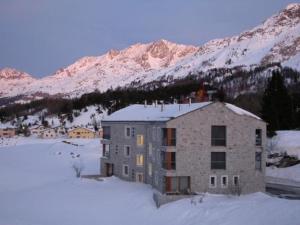 een gebouw in de sneeuw voor een berg bij La Montanella 7 in Maloja