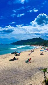 een groep mensen op een strand met parasols en de oceaan bij Pousada Praia do Recreio in Rio de Janeiro