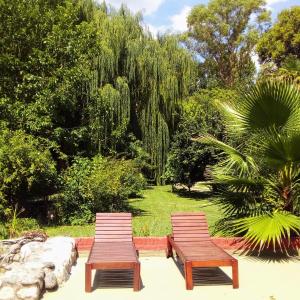 2 bancos de madera sentados en un jardín con árboles en Libertad Posada y Spa en Villa Las Rosas