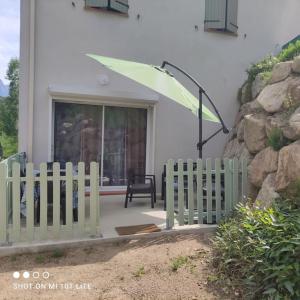 una recinzione bianca di fronte a una casa con un ombrello verde di L'Affacatoghju - Grand studio au village (2p) a Tavera