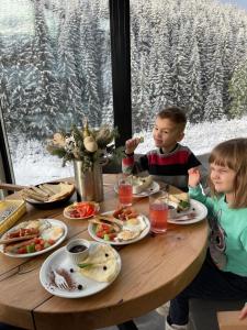 zwei Kinder sitzen an einem Tisch und essen Essen in der Unterkunft Шишка in Bukowel