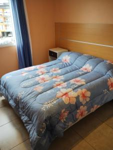 Una cama con un edredón azul con flores. en Cálido departamento en Ushuaia en Ushuaia
