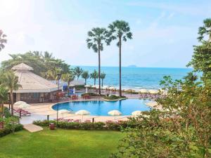 格林的住宿－Novotel Rayong Rim Pae Resort，一座带遮阳伞的游泳池,其背景是大海