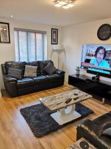 uma sala de estar com um sofá de couro preto e uma televisão em Langley Haven - 3 BR House em Kent