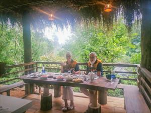 two people sitting at a wooden table with food at Ella nine arch spice garden in Ella