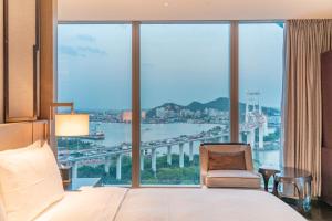ein Schlafzimmer mit einem Bett und einem Stuhl sowie einem großen Fenster in der Unterkunft HUALUXE Xiamen Haicang Habour View - An IHG Hotel in Xiamen
