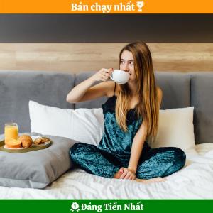 a woman sitting on a bed drinking a cup of coffee at Trang Ngan Hotel by THG in Danang