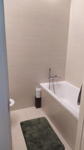 a white bathroom with a tub and a green rug at Apartament Szczęśliwicka in Warsaw