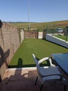 a table and a chair on a patio with a artificial lawn at Agradable casa adosada con piscina in Zahara de los Atunes