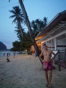 a man standing on the beach next to a palm tree at ALFA Beach Front Lodge in El Nido