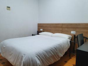 um quarto com uma cama grande com lençóis brancos e almofadas em Hostal Zamorán em Madri