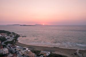 Sunsea Wellness Resort في آغيوس ستيفانوس: غروب الشمس على الشاطئ مع المدينة والمحيط