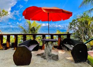 a picnic table with a red umbrella and benches at La Concepcion Cove Garden Resort in Moalboal