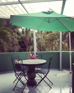 uma mesa e cadeiras debaixo de um guarda-sol verde em Hostel Office- Hospedagem Climatizada quartos e apartamentos privativos em Extrema