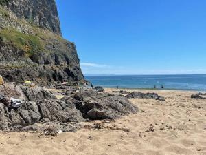 a beach with people in the water and a cliff at Sunnyside at Scurlage Farm in Swansea