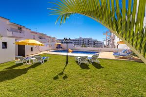 einen Garten mit Stühlen, einem Sonnenschirm und einem Pool in der Unterkunft Apartamentos Carruna in Albufeira