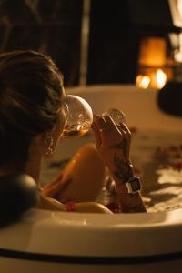 a woman sitting in a bath tub drinking from a wine glass at CASA DE VIDRO EM MEIO A NATUREZA - Conteiner Lua in Piçarras