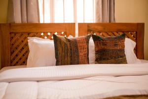 1 cama con almohadas blancas y cabecero de madera en Hecasa Homestay, en Arusha