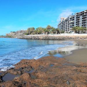 a beach with buildings and palm trees and the ocean at Beachfront apartment Don Paco Patalavaca in Patalavaca