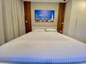 1 cama blanca en un dormitorio con una pintura en la pared en Edifício Loft Apto 501 ER Hospedagens, en Maceió
