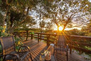 a wooden deck with two chairs and the sun setting at Rosa Casa Vivendas da Colina in Canela