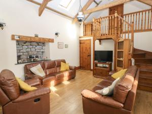 a living room with leather furniture and a wooden staircase at The Old Cow Barn in Llansadurnen