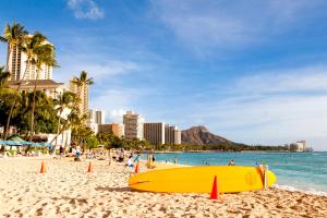 una tabla de surf amarilla sentada en una playa con gente en Aqua Palms Renovated 1BR, City View, Swimming Pool en Honolulu