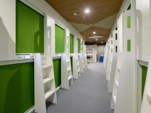 um corredor com paredes verdes e prateleiras brancas em Tabist カプセルイン笠懸 男性専用 Tabist Capsule Inn Kasakake Male Only em Midori