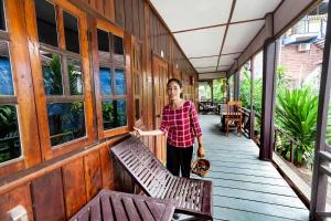 una mujer parada en un porche con bancos en Lao Long Riverside and Budget Garden Guesthouse, en Ban Khon